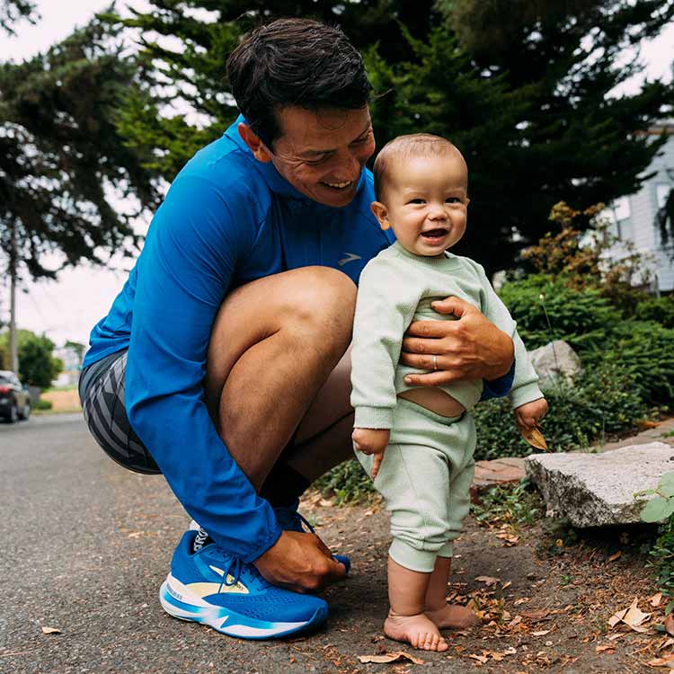 A man and a baby stand together, smiling, in a green park.